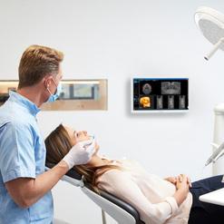 Zahnarzt untersucht Patientin im Behandlungsstuhl, monitor zeigt Röntgenbilder im Hintergrund.