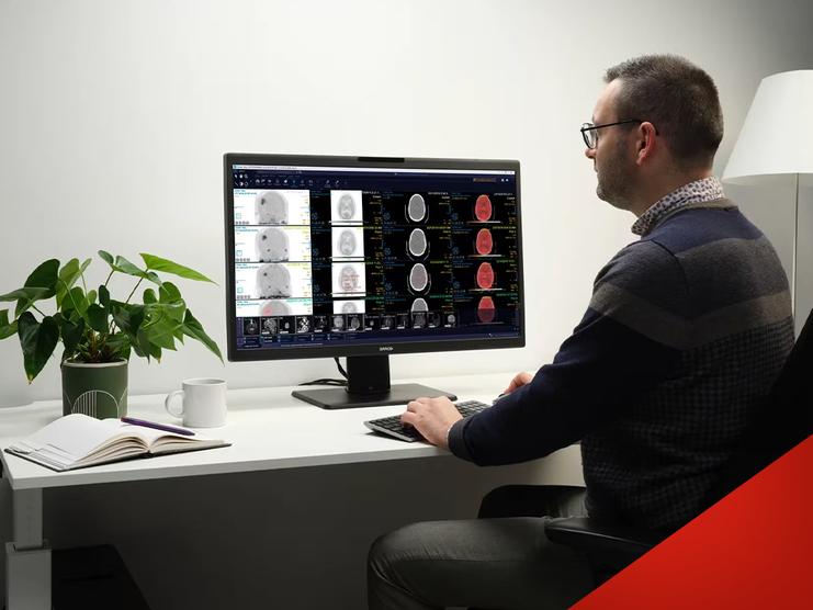 Mann analysiert medizinische Bildgebung auf einem Monitor, w&auml;hrend er an einem Schreibtisch mit Pflanzen arbeitet.