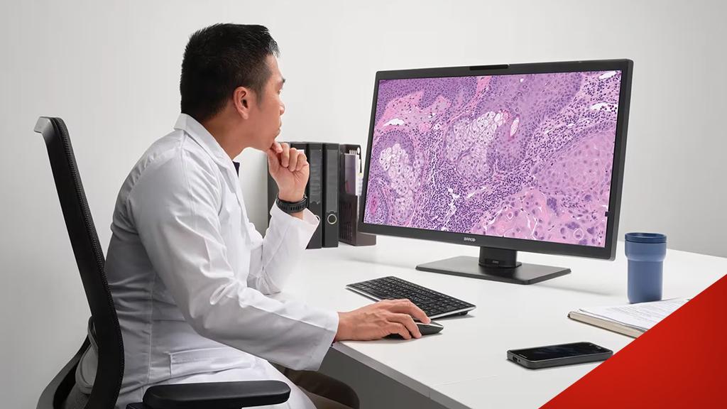 Ein Arzt in Weiß untersucht am Computerbildschirm ein histologisches Bild mit rosa Gewebestrukturen.